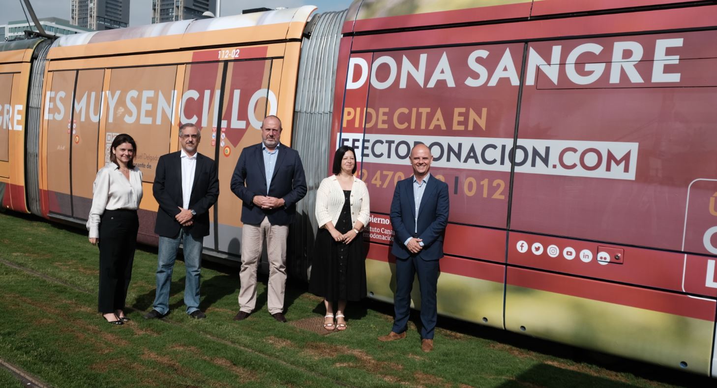 Autoridades de Metrotenerife, del Instituto Canario de Hemodonación y Hemoterapia, de Titsa y Publiservic junto a tranvía rotulado.